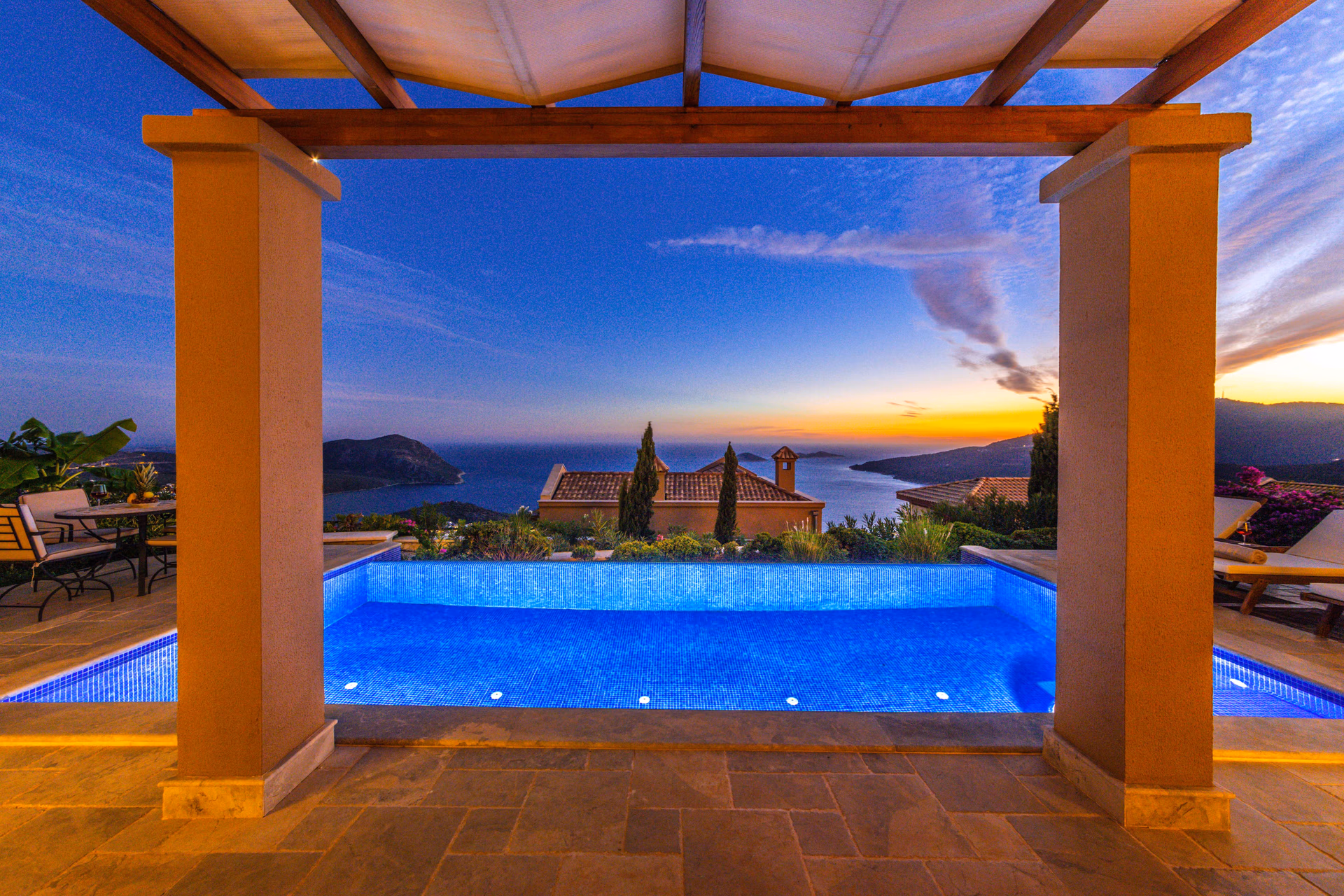 Illuminated pool and terrace overlooking the sea at dusk