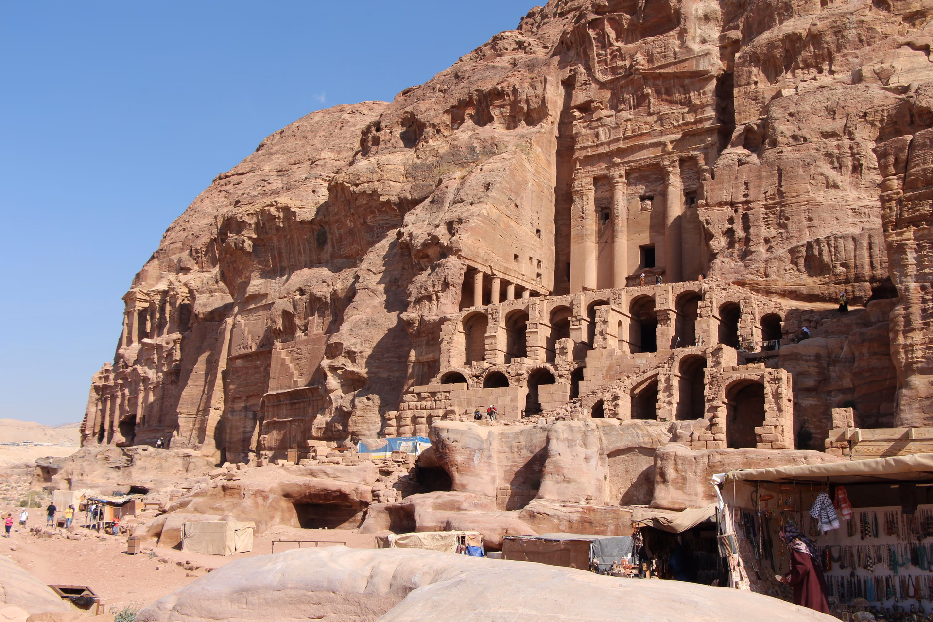 Rock-cut tomb facades in Petra with small groups of visitors and market stalls