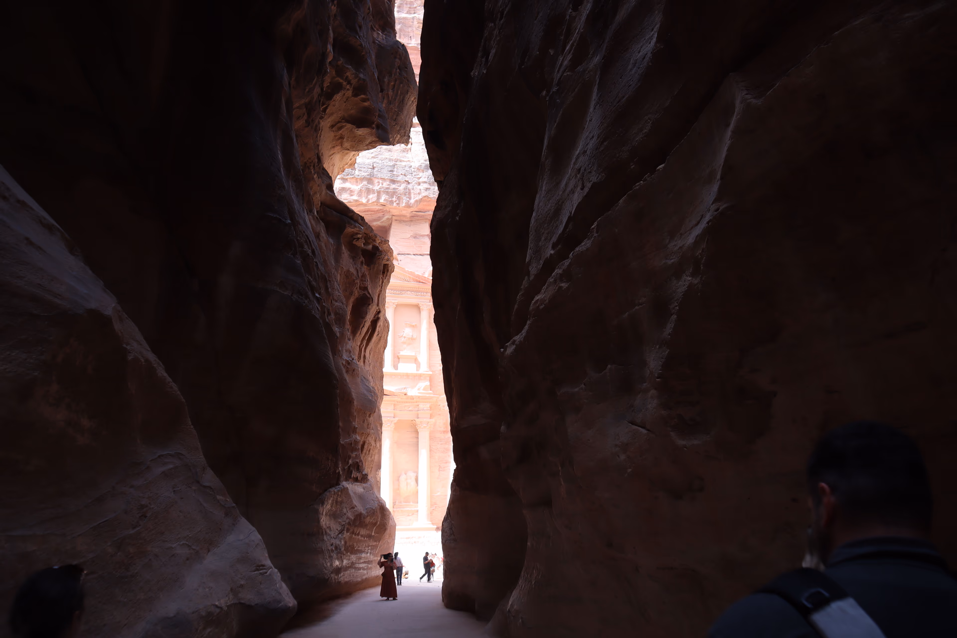 Visitors walking through the narrow Siq rock gorge toward the carved Treasury facade at Petra