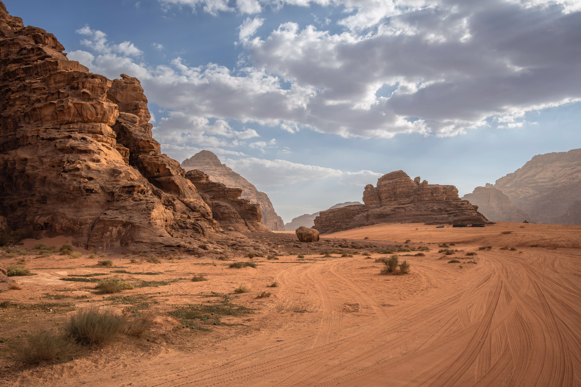 Red sandstone cliffs, desert tracks and sparse scrub beneath a dramatic cloudy sky in Jordan